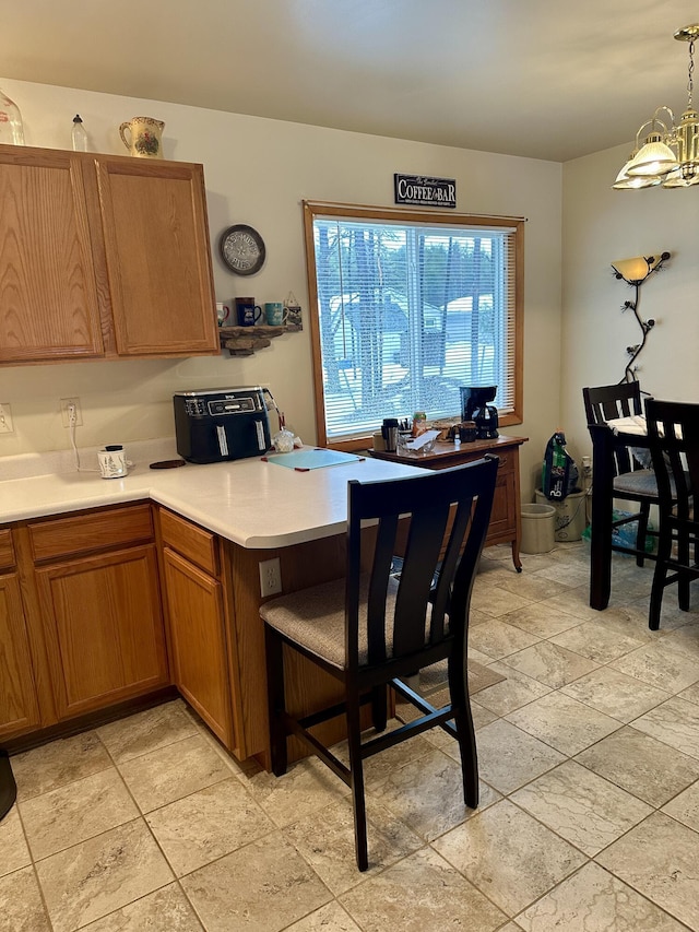 kitchen with a peninsula, brown cabinets, light countertops, and a chandelier