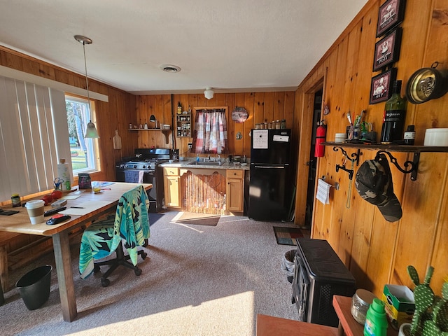 interior space featuring wooden walls, range with gas cooktop, black refrigerator, decorative light fixtures, and carpet floors