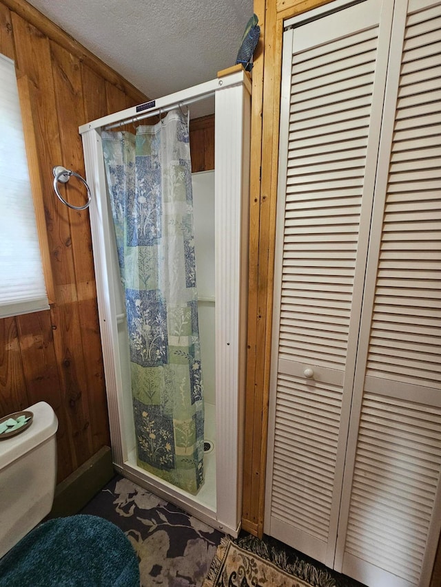 bathroom featuring curtained shower, toilet, wooden walls, and a textured ceiling