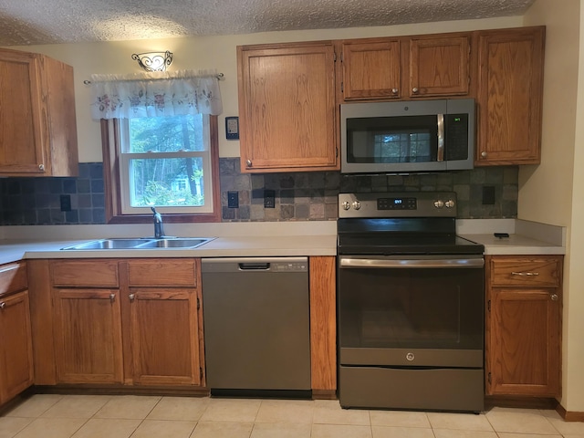 kitchen with sink, tasteful backsplash, a textured ceiling, light tile patterned floors, and appliances with stainless steel finishes