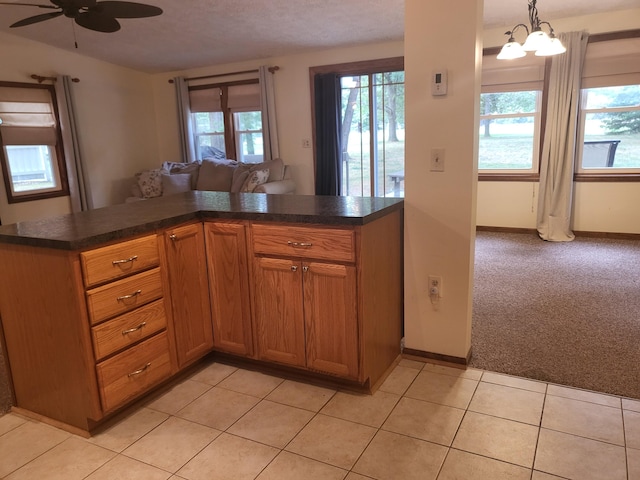 kitchen featuring ceiling fan with notable chandelier, light colored carpet, kitchen peninsula, and hanging light fixtures