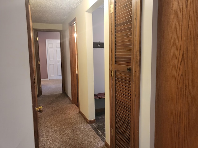 hallway with dark carpet and a textured ceiling