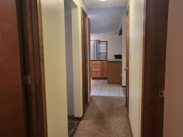 hall featuring vaulted ceiling, light tile patterned flooring, and a textured ceiling