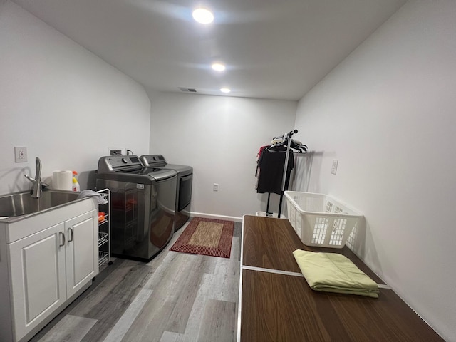 clothes washing area featuring hardwood / wood-style flooring, cabinets, washing machine and dryer, and sink