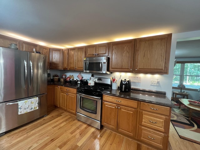 kitchen with light wood-type flooring, stainless steel appliances, and dark stone counters