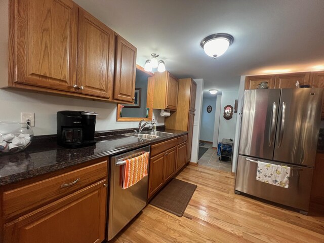 kitchen with dark stone countertops, appliances with stainless steel finishes, sink, and light hardwood / wood-style floors