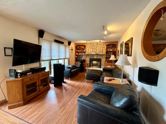 living room with a textured ceiling, wood-type flooring, built in shelves, and a stone fireplace