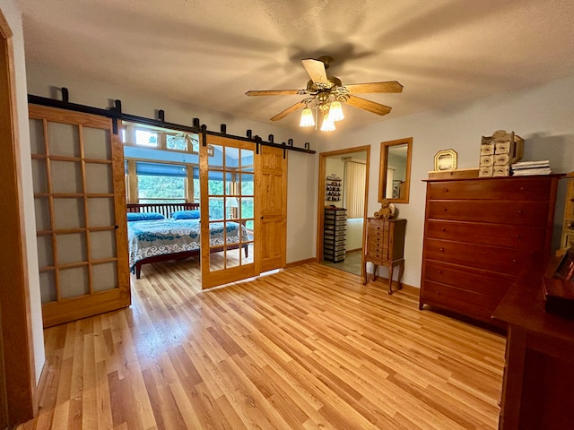 unfurnished bedroom featuring a textured ceiling, light hardwood / wood-style flooring, ceiling fan, and a barn door