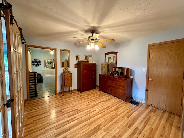 bedroom with ensuite bath, a textured ceiling, light hardwood / wood-style flooring, and ceiling fan