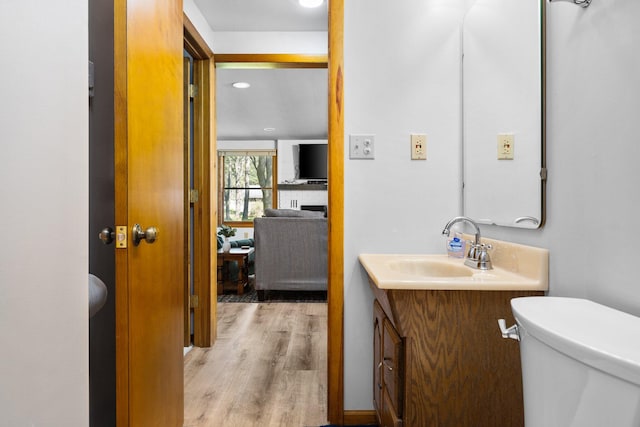 bathroom with a brick fireplace, vanity, hardwood / wood-style floors, and toilet