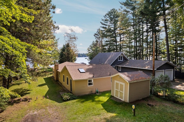 exterior space featuring a garage, a yard, a water view, and an outbuilding