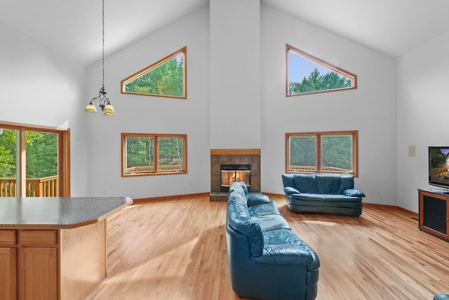 living room featuring light hardwood / wood-style flooring, a tiled fireplace, high vaulted ceiling, and an inviting chandelier