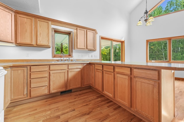 kitchen with light hardwood / wood-style flooring, hanging light fixtures, kitchen peninsula, sink, and a chandelier