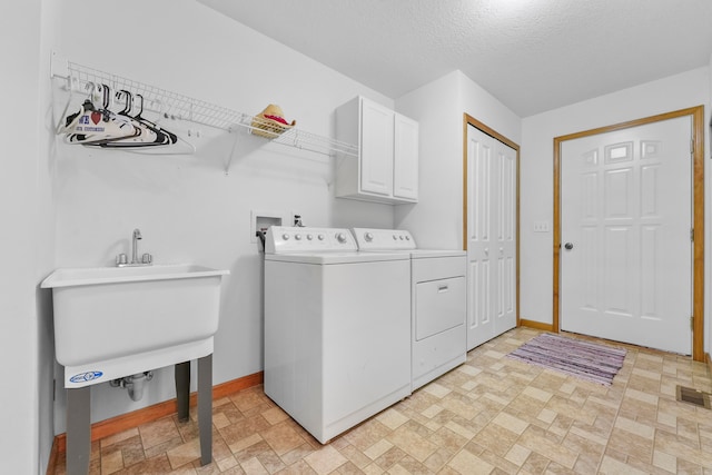 clothes washing area featuring a textured ceiling, cabinets, washing machine and dryer, and sink