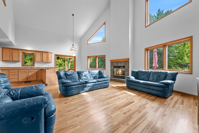 living room with a tiled fireplace, sink, high vaulted ceiling, and light hardwood / wood-style floors