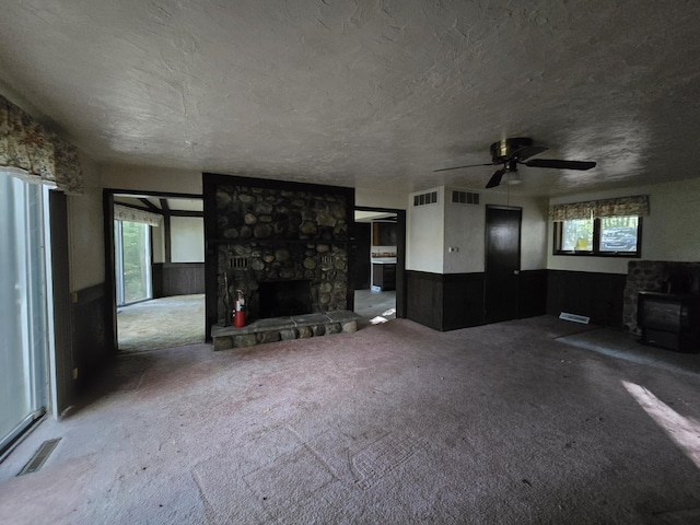 living room featuring light carpet, a textured ceiling, a stone fireplace, and ceiling fan