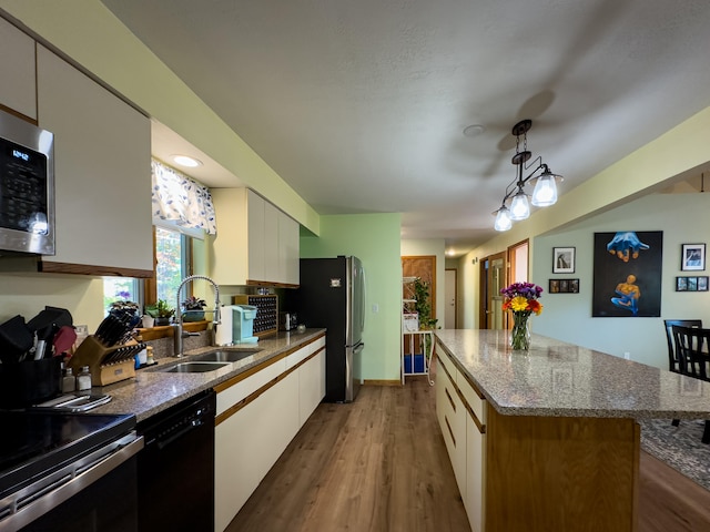 kitchen featuring sink, hanging light fixtures, appliances with stainless steel finishes, a kitchen island, and white cabinets