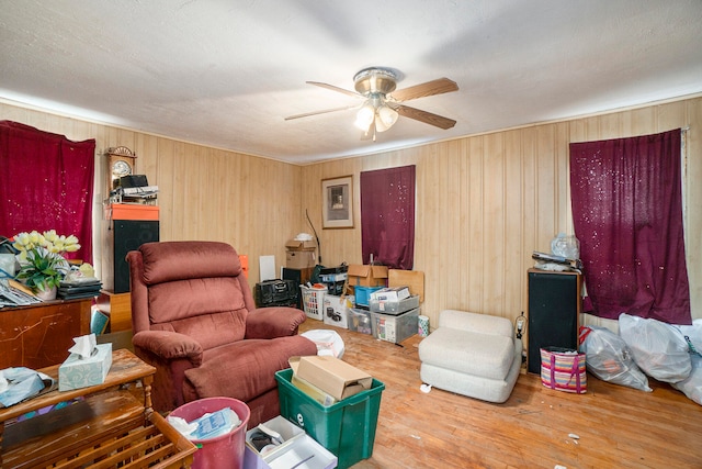 living room featuring hardwood / wood-style floors, ceiling fan, wood walls, and a textured ceiling