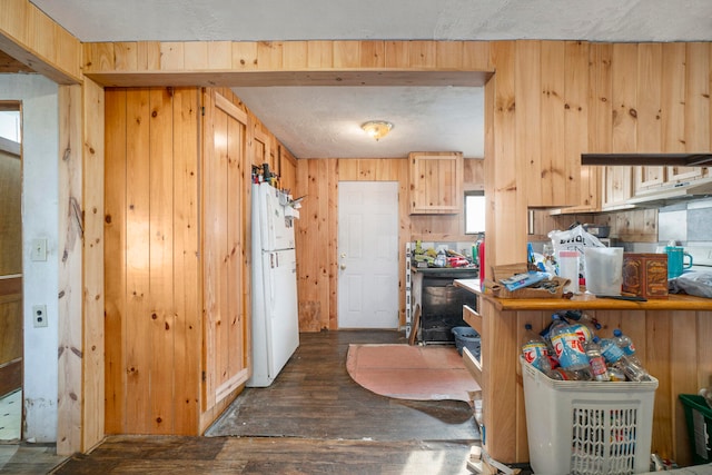 kitchen featuring wooden walls, a textured ceiling, dark wood-type flooring, white refrigerator, and light brown cabinets