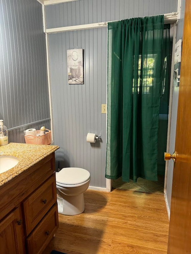 bathroom with toilet, wood walls, hardwood / wood-style floors, vanity, and curtained shower