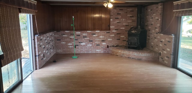 unfurnished living room with ceiling fan, light hardwood / wood-style flooring, brick wall, and a wood stove