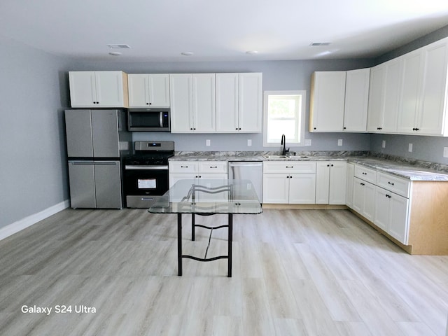 kitchen featuring appliances with stainless steel finishes, white cabinetry, sink, and light hardwood / wood-style flooring