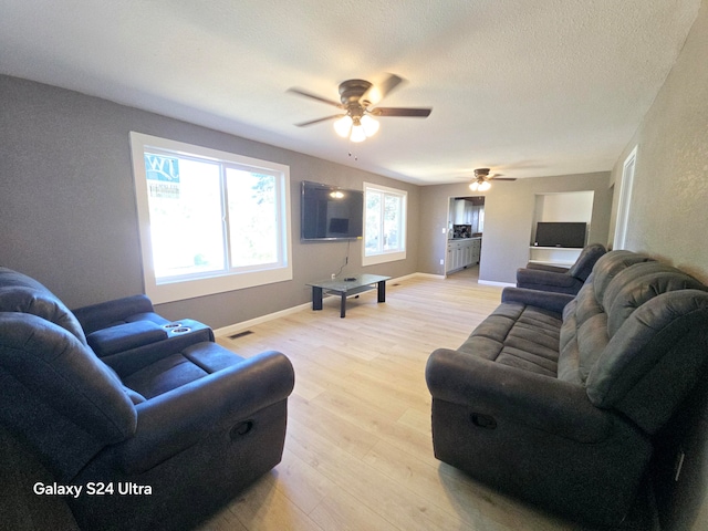 living room featuring light wood-type flooring, ceiling fan, and a textured ceiling