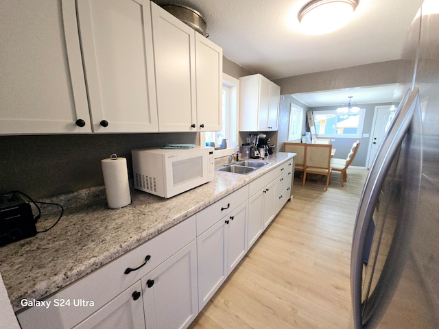 kitchen with light wood-type flooring, a chandelier, light stone counters, sink, and white cabinets