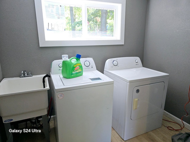 clothes washing area with light wood-type flooring, sink, and washing machine and dryer