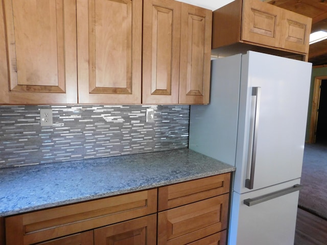 kitchen with light stone countertops, white fridge, tasteful backsplash, and dark wood-type flooring