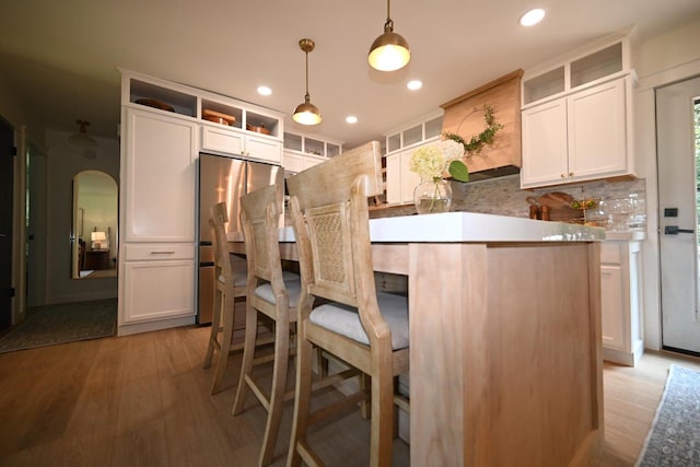 kitchen with pendant lighting, stainless steel fridge, light hardwood / wood-style flooring, white cabinetry, and a center island