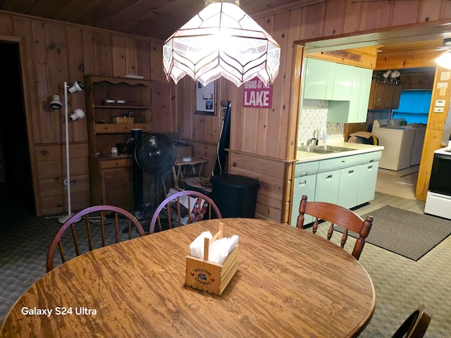 carpeted dining area featuring wood walls, independent washer and dryer, and sink