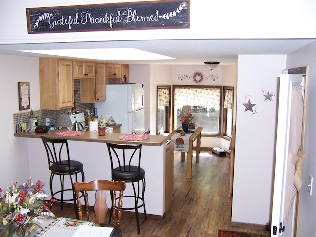 kitchen with tasteful backsplash, kitchen peninsula, a breakfast bar area, white fridge, and dark hardwood / wood-style floors