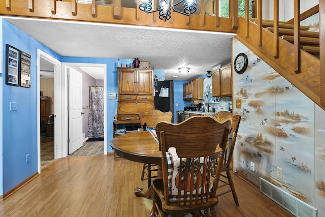 dining area with an inviting chandelier, a textured ceiling, and light hardwood / wood-style floors