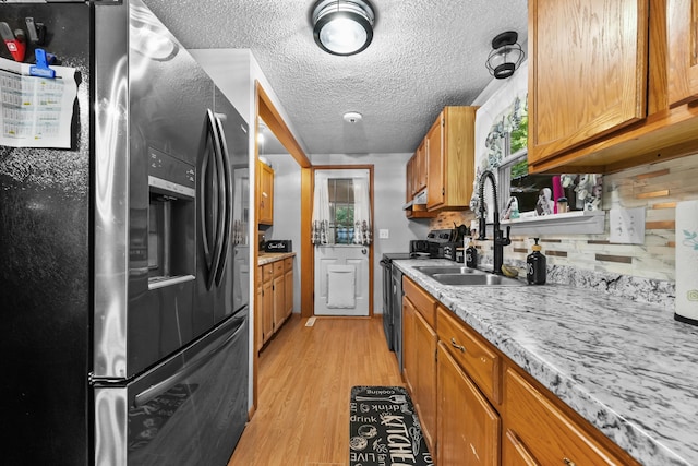 kitchen with tasteful backsplash, light stone countertops, light hardwood / wood-style flooring, stainless steel refrigerator with ice dispenser, and sink