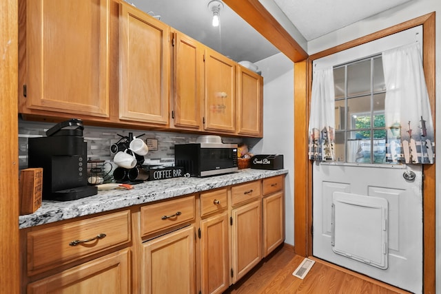 kitchen with light stone counters, light hardwood / wood-style flooring, and decorative backsplash