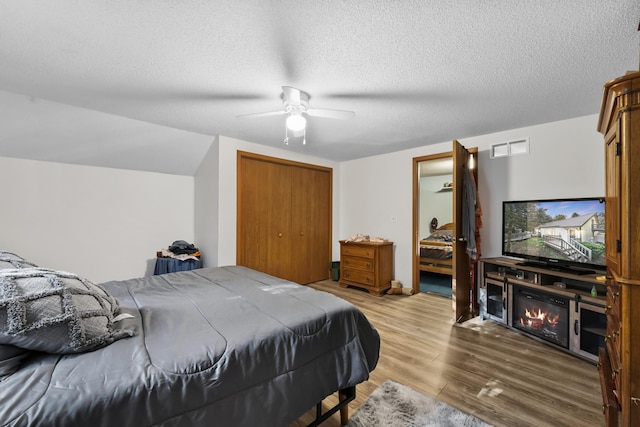 bedroom with light wood-type flooring, a textured ceiling, ceiling fan, and a closet