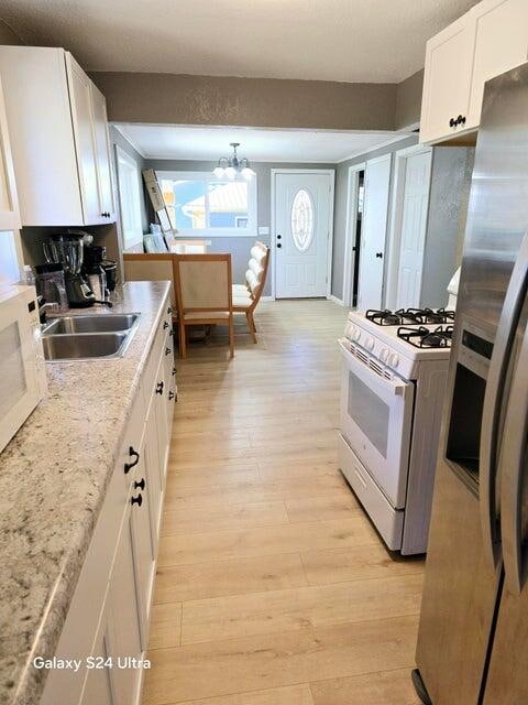 kitchen with white cabinetry, white appliances, light wood-type flooring, sink, and a notable chandelier