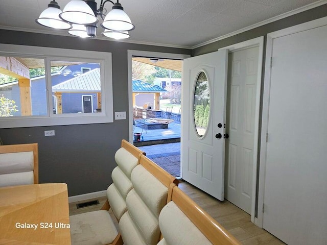 entrance foyer with light wood-type flooring, ornamental molding, and an inviting chandelier