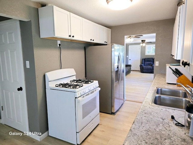 kitchen featuring white gas range oven, sink, white cabinetry, light hardwood / wood-style flooring, and ceiling fan