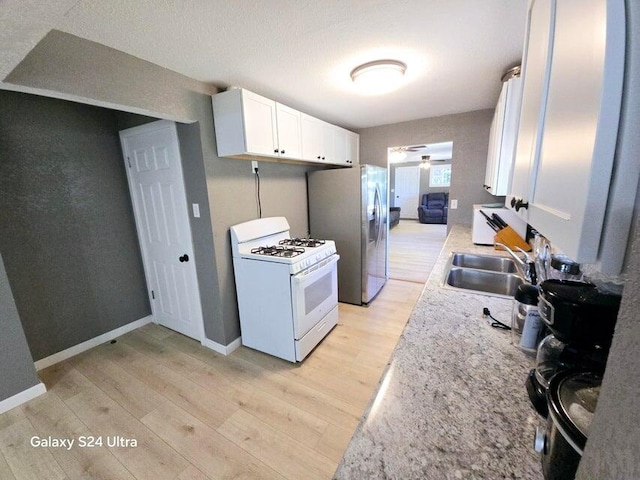 kitchen with white cabinetry, white appliances, light hardwood / wood-style flooring, ceiling fan, and sink