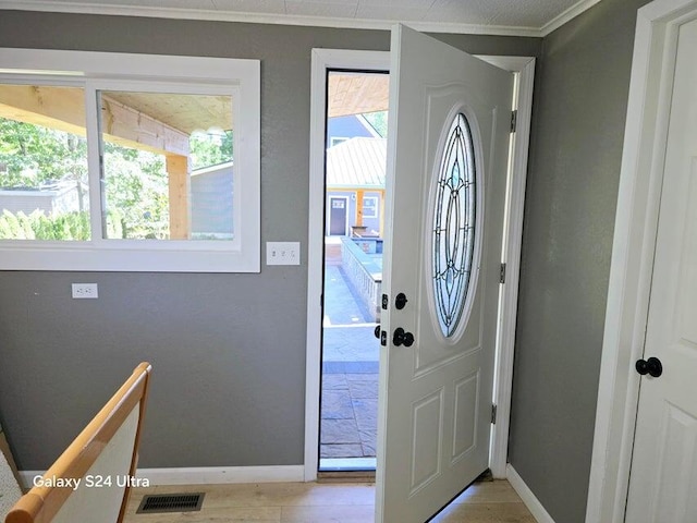 foyer featuring light wood-type flooring, plenty of natural light, and crown molding