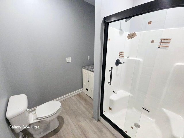 bathroom with wood-type flooring, a shower with door, vanity, and toilet