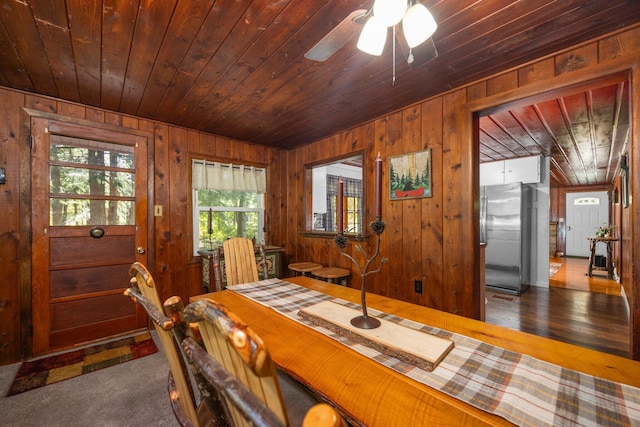 dining area with wood walls, ceiling fan, wood ceiling, and dark colored carpet