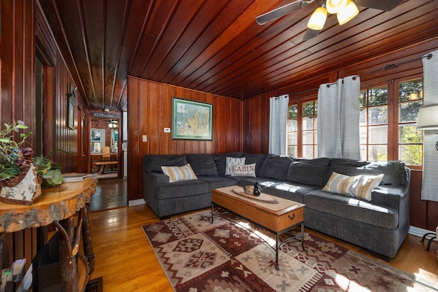 living room featuring ceiling fan, wood walls, light wood-type flooring, and wooden ceiling