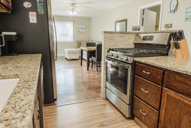 kitchen with light hardwood / wood-style flooring, light stone counters, ceiling fan, and stainless steel range with gas stovetop