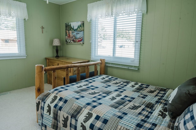 carpeted bedroom featuring wood walls and multiple windows