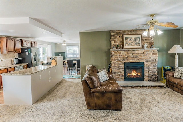 living room featuring a stone fireplace, light colored carpet, and ceiling fan