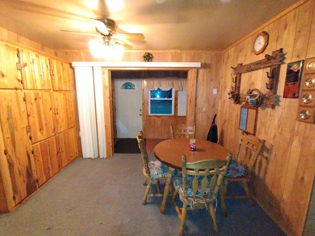 dining space with ceiling fan, light carpet, and wooden walls