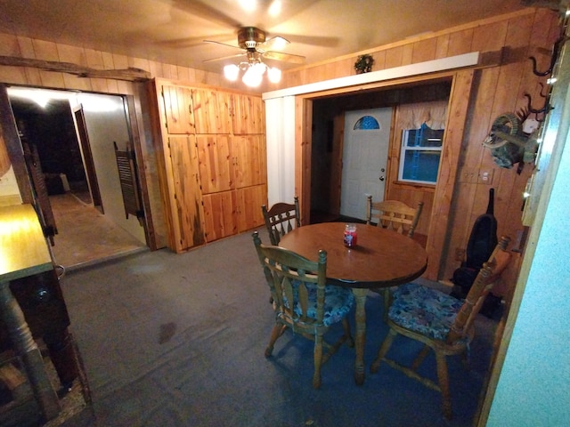 carpeted dining room with ceiling fan and wood walls